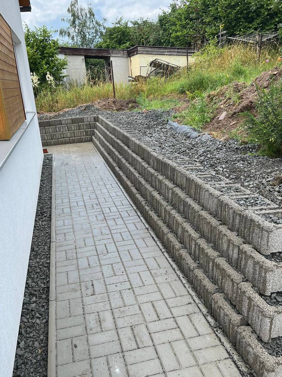 Chodník ze zámkové dlažby podél domu a terasovitá opěrná zeď z betonových tvárnic