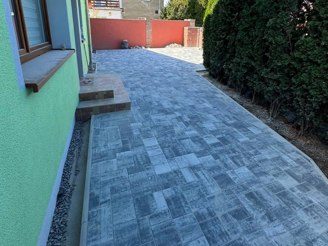Nový dvůr a chodník podél domu ze šedé melírované zámkové dlažby
